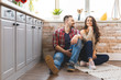 © denis_vermenko - Young man and woman sitting on floor in kitchen and talking. Loving young couple spending time together at home.