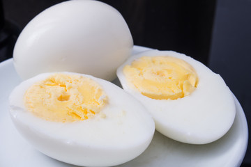 one boiled egg cut in half on a white plate and black background