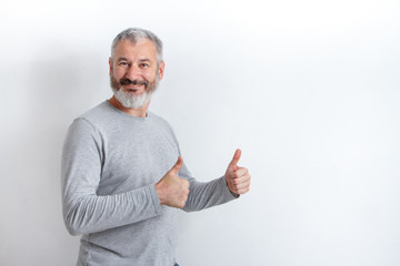 Wall Mural - Adult happy gray-haired man with a beard showing thumbs up on a white background, free method for text