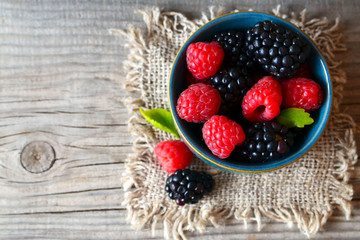 Fresh ripe organic blackberries and raspberries in a blue bowl on rustic wooden table.Summer berries.Healthy eating,vegan food or diet concept. Selective focus.