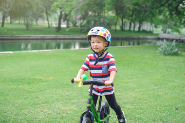 Wall Mural - Cute little Asian toddler boy child wearing safety helmet learning to ride first balance bike in sunny summer day, kid playing & cycling at park