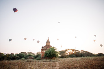 Hot air balloon over the foggy morning around Temple in Bagan, Myanmar. Balloons fly over thousands of ancient pagodas. Dawn in Bagan, misty. Tourists are watching the sunrise over the ancient city.