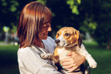 Wall Mural - Girl holding a dog in her arms on the nature background at summer time. Lifestyle photo.