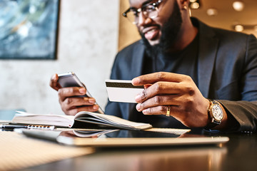 shot of african american businessman holding mobile and credit card, while resting in the cafe