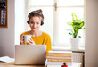 © Halfpoint - A young female student sitting at the table, using headphones when studying.