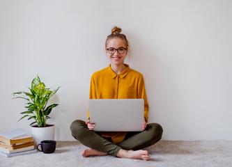 Poster - A young female student sitting on floor using laptop when studying.