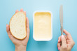 Woman's hands holding slice of white bread and knife. Opened plastic pack of light yellow margarine on pastel blue desk. Preparing breakfast. Point of view shot. Closeup.