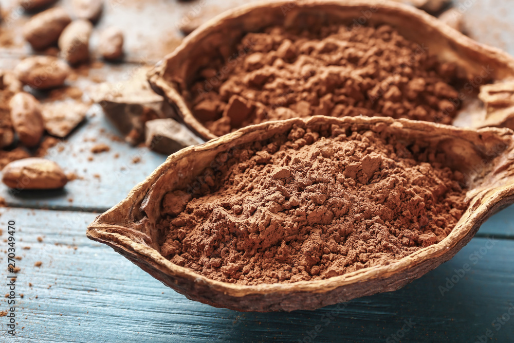 Pods with cocoa powder on wooden background, closeup