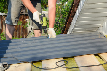 Sticker - Roofer with crew gun installing metal roof tiles. Roofing construction with roofing contractor laying metal roof sheets.