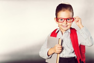 Cute little schoolgirl in glasses with book on  background