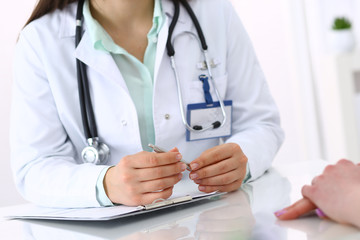 Unknown doctor and patient talking while sitting at the desk in hospital office, close-up of human hands. Medicine and health care concept