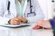 © rogerphoto - Doctor and patient talking while sitting at the desk in hospital office, close-up of human hands. Medicine and health care concept