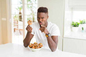 Poster - African american man eating chocolate chips muffin pointing with finger to the camera and to you, hand sign, positive and confident gesture from the front