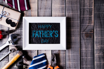 Happy fathers day concept. Top view of white picture frame with border of tools and ties, retro f glasses on dark wooden table background. Flat lay.