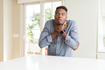 Poster - Handsome african american man on white table shouting and suffocate because painful strangle. Health problem. Asphyxiate and suicide concept.