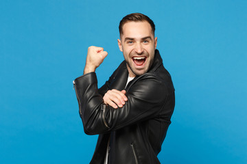 Stylish young bearded man in black leather jacket white t-shirt showing biceps, muscles isolated on blue wall background studio portrait. People sincere emotions lifestyle concept. Mock up copy space.