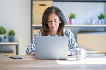 Poster - Middle age senior woman sitting at the table at home working using computer laptop Relaxed with serious expression on face. Simple and natural looking at the camera.