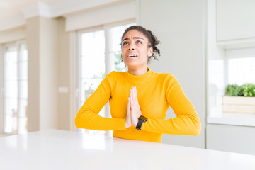 Sticker - Beautiful african american woman with afro hair wearing a casual yellow sweater begging and praying with hands together with hope expression on face very emotional and worried. Asking for forgiveness