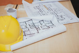 Fototapeta  - Cropped shot of a workplace of professional engineer. Yellow protective hardhat and architectural blueprints on the desk, copy space