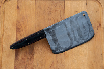 The meat cleaver is a multi use kitchen or butcher knife that resembles a rectangular bladed hatchet. This one is made of a damascus steel blade and sits on a cutting board. Bokeh effect.