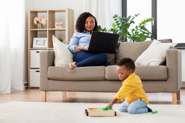 family, motherhood and people concept - happy african american mother using laptop computer and little baby son playing with toy blocks kit at home