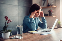 Woman With Headache And Capsules With Glass Of Water On A Office Desk