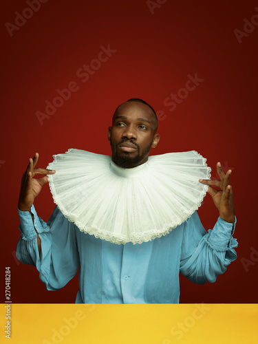 Fotomural Young man as a medieval grandee or nobleman on red studio background