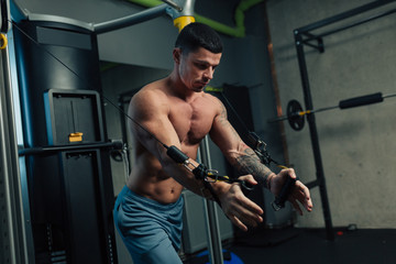 Young strong man in gym doing chest cable workout