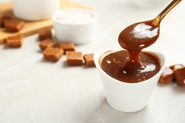 Spoon with tasty caramel sauce over bowl on table. Space for text