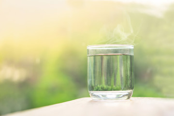 glass of hot or warm water with smoke on wooden table with nature background 