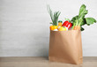 Paper bag with vegetables and bottle of juice on table against grey background. Space for text