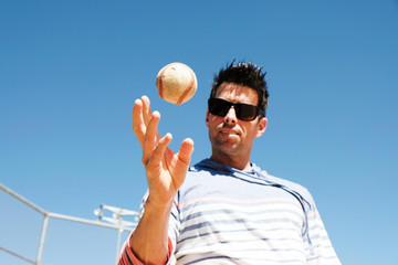 Canvas Print - Baseball player in casual attire playing with ball on sunny day outside.