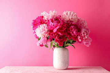 Wall Mural - Vase with bouquet of beautiful peonies on pink table against color background, space for text