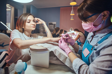 Wall Mural - Attractive young woman with tattoo is getting nail care from expirienced manicurist.