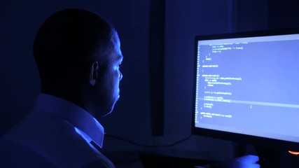 Portrait of african american man programmer coding network security software. Hacker typing code on computer screen in dark office at night