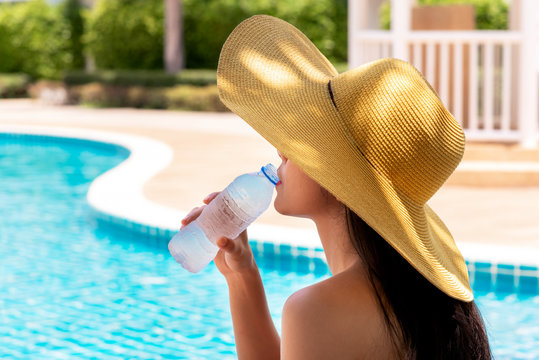 Women have long hair, wearing a big hat Drinking cold water from plastic bottles Near the pool, to summer concept.