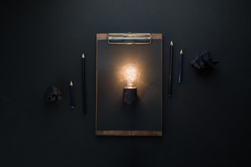 Light bulb shining in flat lay with crumpled paper balls and a clipboard. The idea for engineering, building or construction concept with copy space.