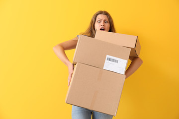 Shocked woman with cardboard boxes on color background