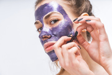 young girl with beautiful face removes a purple cosmetic mask. Close-up. Macro.