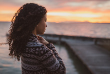 Thoughtful Evening Mood With A Young African American Woman Standing On The Promenade By The Lake And Looking Towards The Water And The Setting Sun. Burning Sky