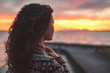 © JürgenBauerPictures - Afro American woman standing on the promenade by the lake and looking towards the water and the setting sun. Burning sky. Thoughfull moment