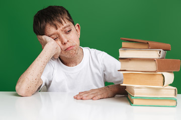 Tired young boy with freckles sleeping while sitting by table