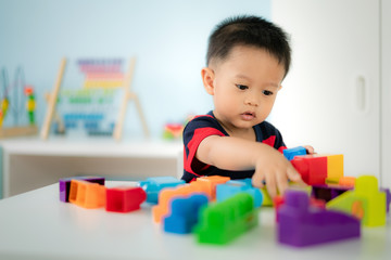 adorable asian toddler baby boy sitting on chair and playing with color block toys at home..
