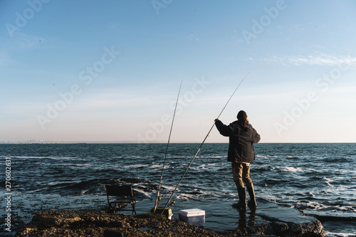 Fotomural Handsome young man fisherman wearing coat and hat at the seashore
