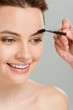 © LIGHTFIELD STUDIOS - cropped view of makeup artist holding eyebrow brush near cheerful naked woman isolated on grey