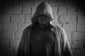 Black and white photo of a man in a cardigan with a hood on his head against a brick wall