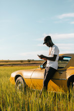 Black African Man Besides A Classic Car Using A Mobile Phone