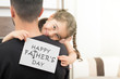 girl hugging her father and showing happy father's day card