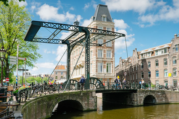 Wall Mural - Amsterdam, Netherlands - metal drawbridge with people passing by and bicycles resting on the railing