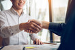 © wutzkoh - Entrepreneurs collaboration deal shaking hands in a modern office and financial paper graph on desk.